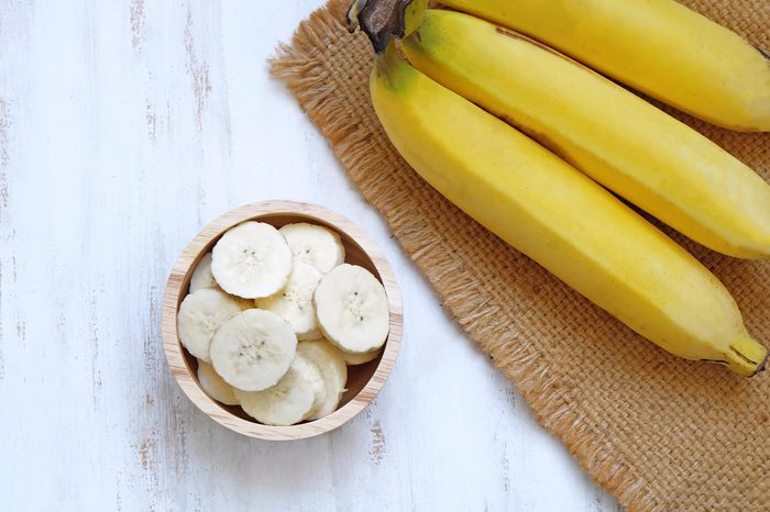 Bowl of sliced bananas next to bunch of bananas