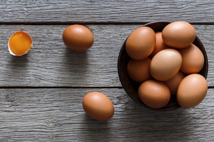 Fresh chicken brown and white home eggs with cracked eggshell and yolk in bowl at rustic wood table. Top view with copy space. Rural still life, natural healthy food and organic farming concept.