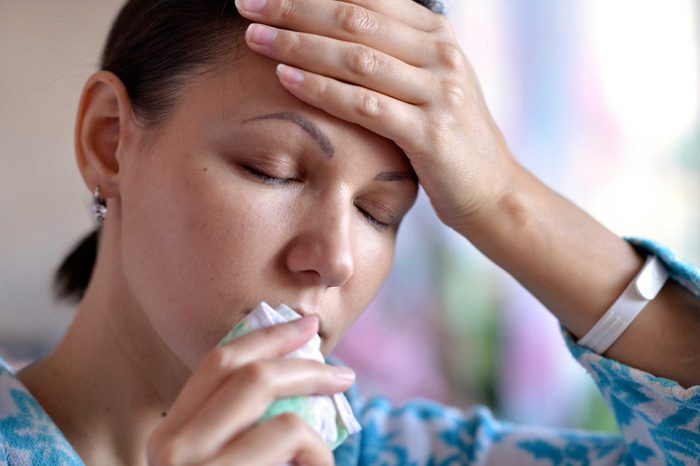 A woman holding her forehead in her left hand and a tissue to her mouth.