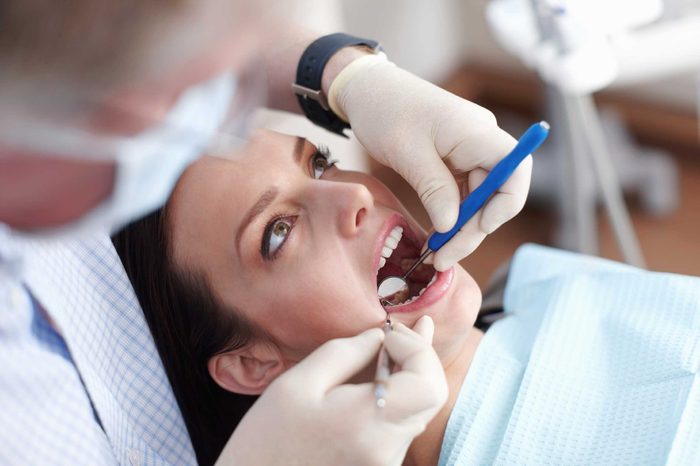 Woman dental patient opening her mouth while her dentist inspects her teeth with a hand mirror.