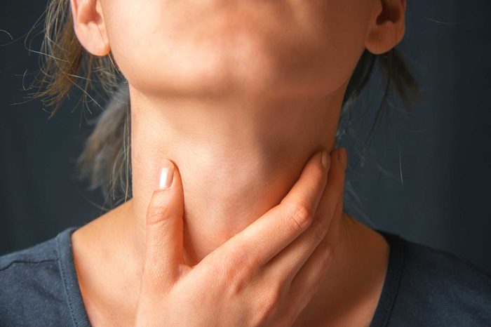 A woman wearing a T-shirt and holding her throat in her right hand as if in pain.