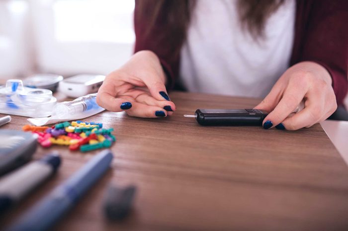 Woman sitting at a table checking her blood glucose levels with a glucose monitor.