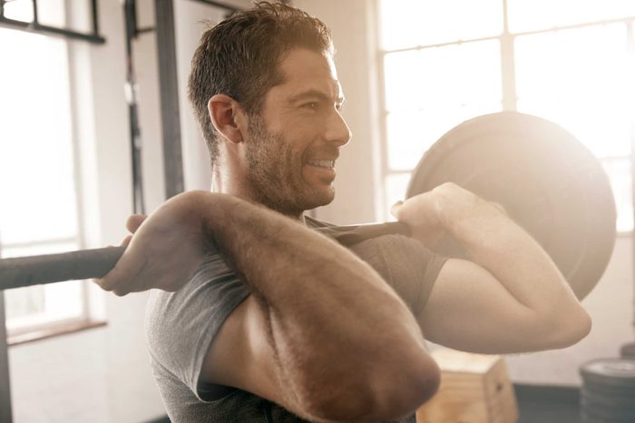 Man exercising in a gym, holding a weighted barbell against his chest.