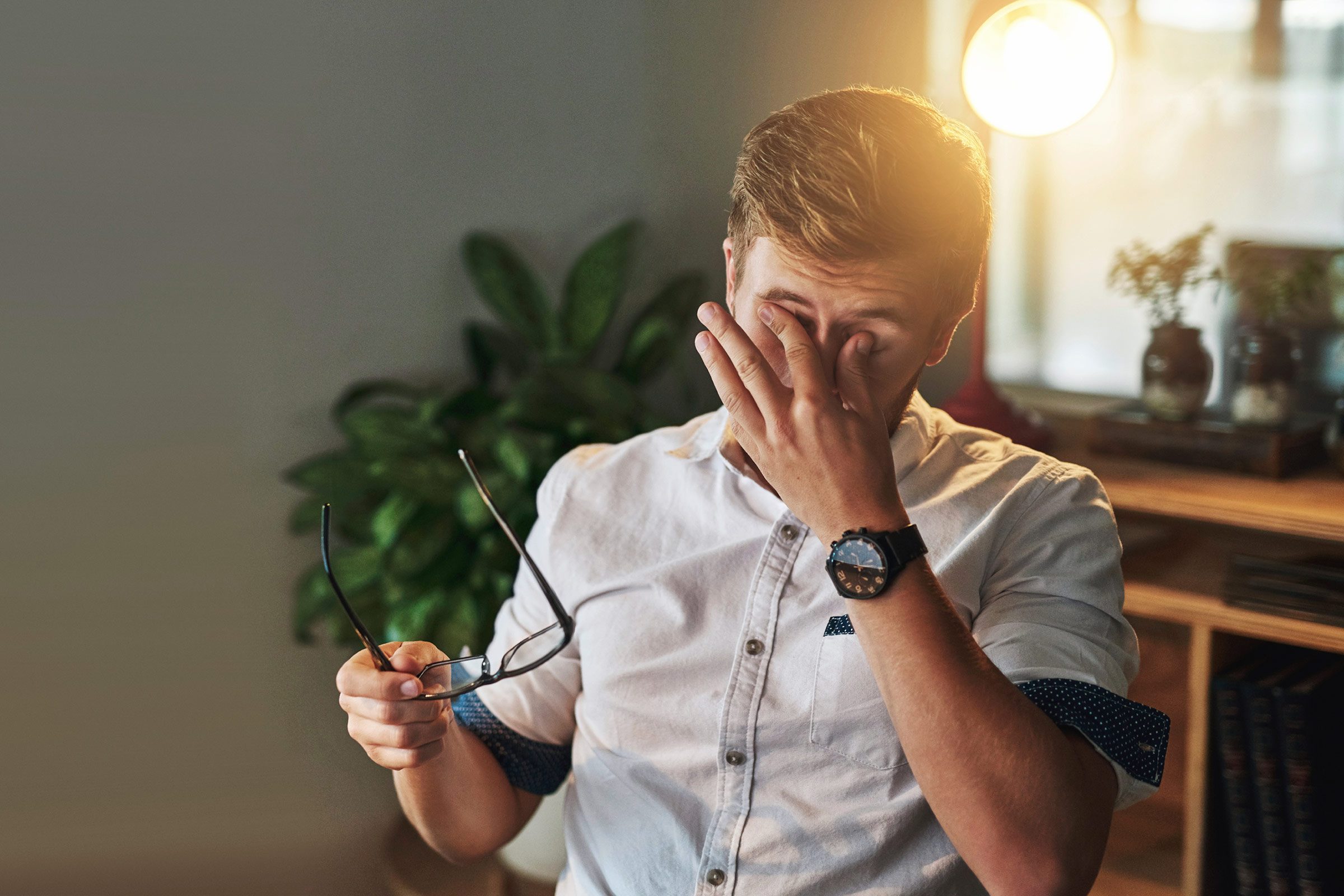 man holding his glasses while he rubs his eyes