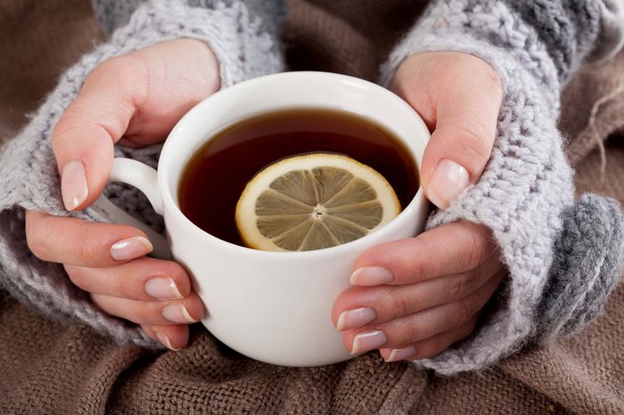 Woman in a sweater holding a cup of tea with a lemon slice.