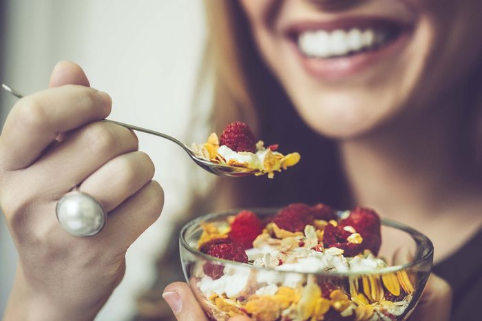 Woman eating yogurt with cereal and raspberries