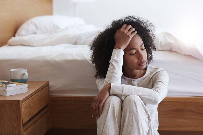 Woman sitting on the floor beside her bed