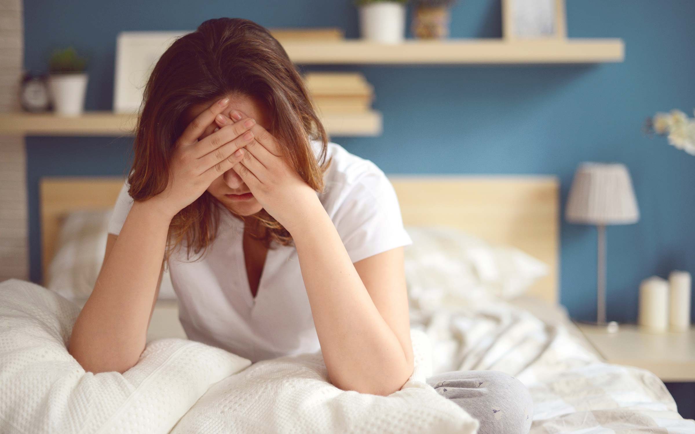 woman sitting in bed, holding head in hands and looking distressed