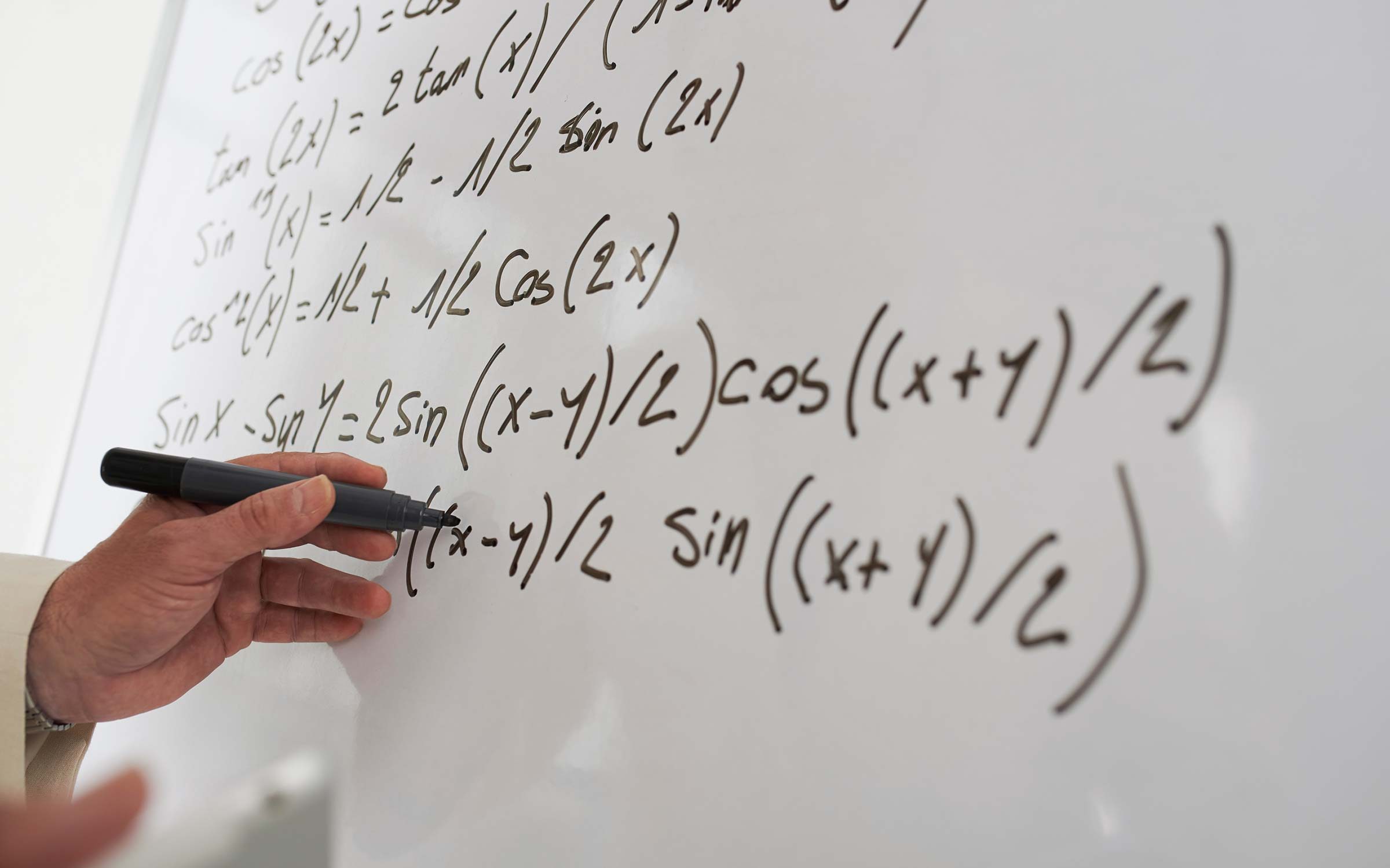 hand holding a pen and doing equations on a whiteboard