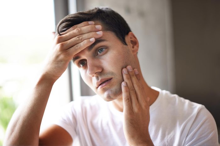 Man in a white shirt holding his forehead and rubbing the skin on his cheek.