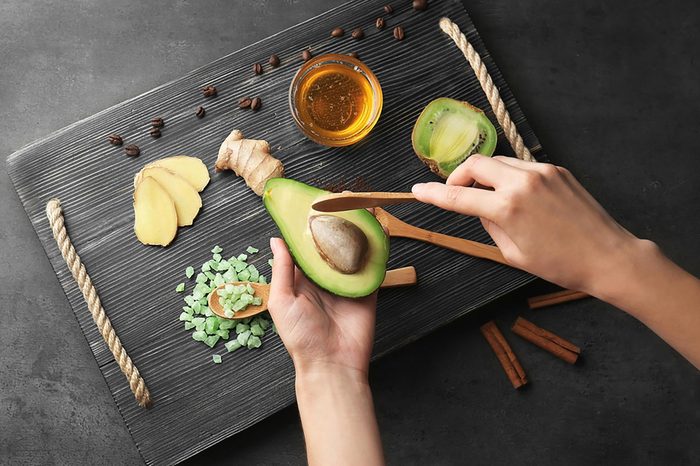 woman scooping avocado; tray of ginger, honey, and other natural items in background