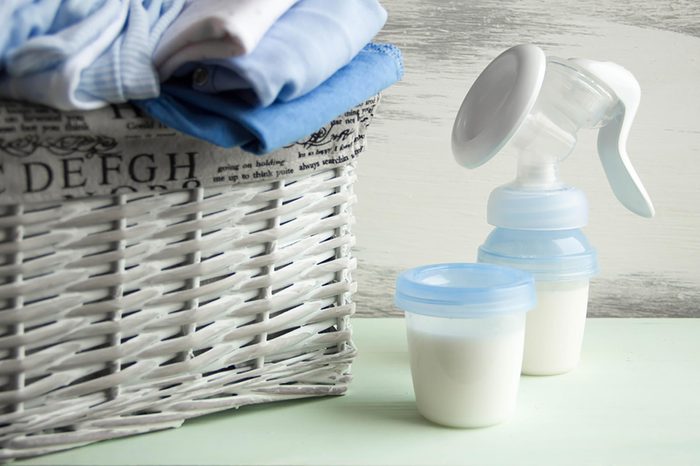 breast hand pump and breastmilk next to basket of onesies