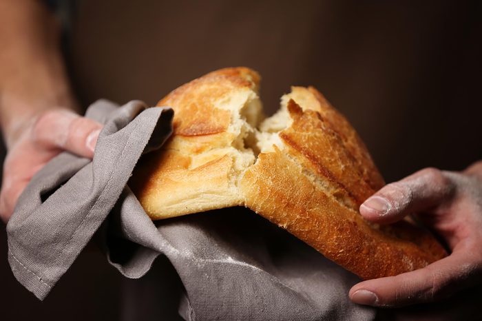 person breaking a loaf of crusty bread in half