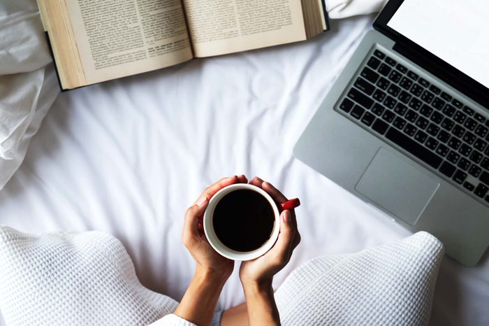 Hands holding coffee with computer and book