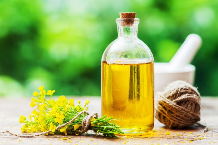 Glass vial of olive oil next to sprig of yellow flowers