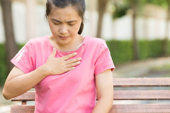 Asian woman holding her hand to her chest with a pained expression