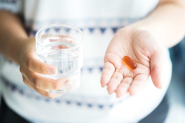 woman holding a glass of water in one hand, supplement in the other