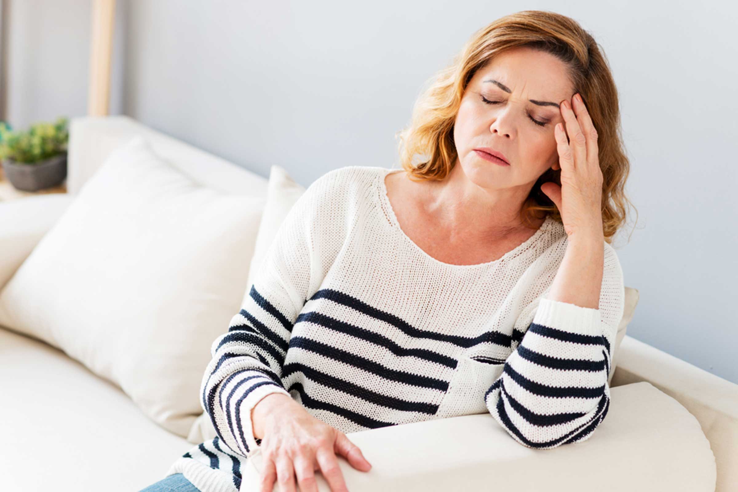 woman on couch in pain, holding her head