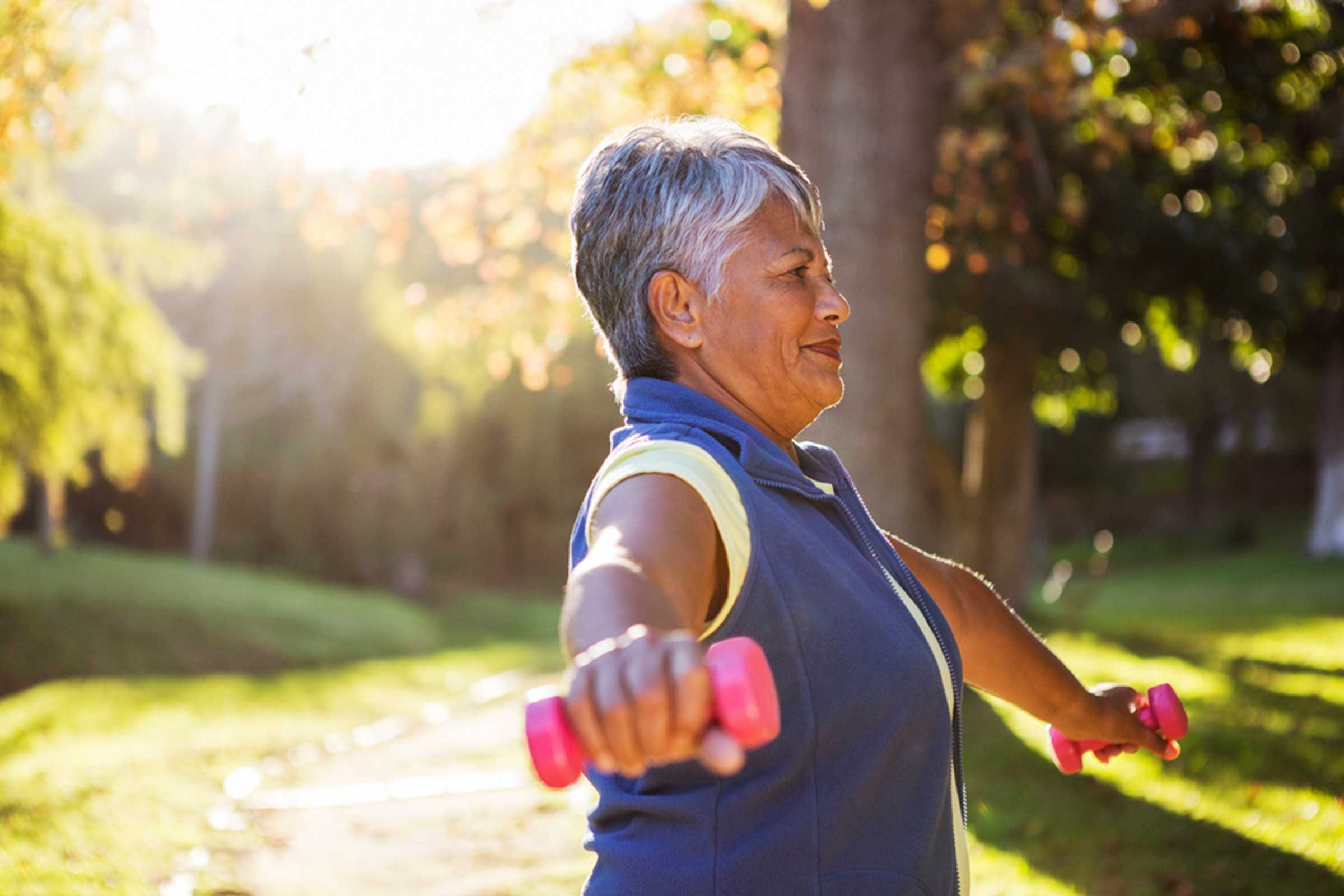 woman lifting small dumbbells in a park