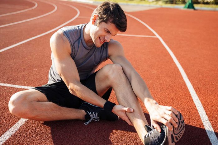 Man in workout gear stretching his leg as if having a cramp.