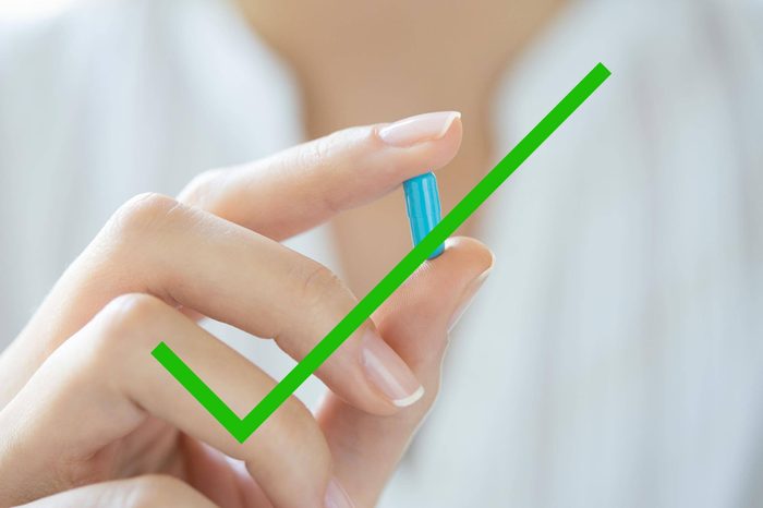 A woman holding a laxative pill in her fingers with a check through it.