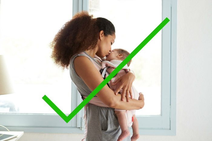 Woman holding a baby in front of a window.