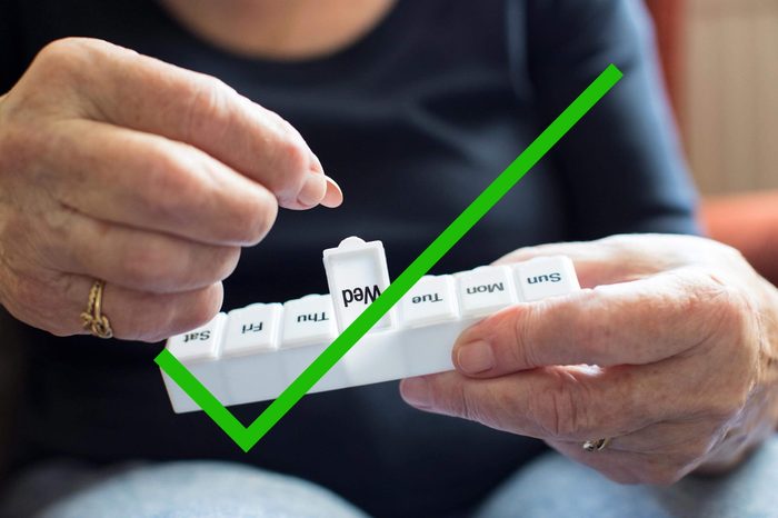 Person putting medication in a pill box with a check through it.