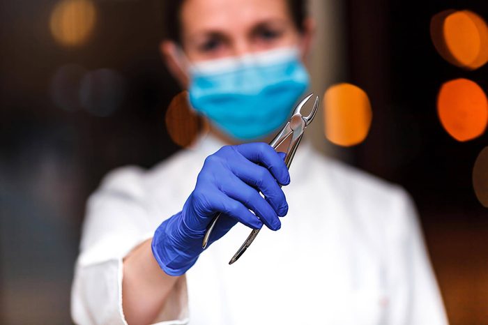 dentist looking into camera holding a tooth extractor