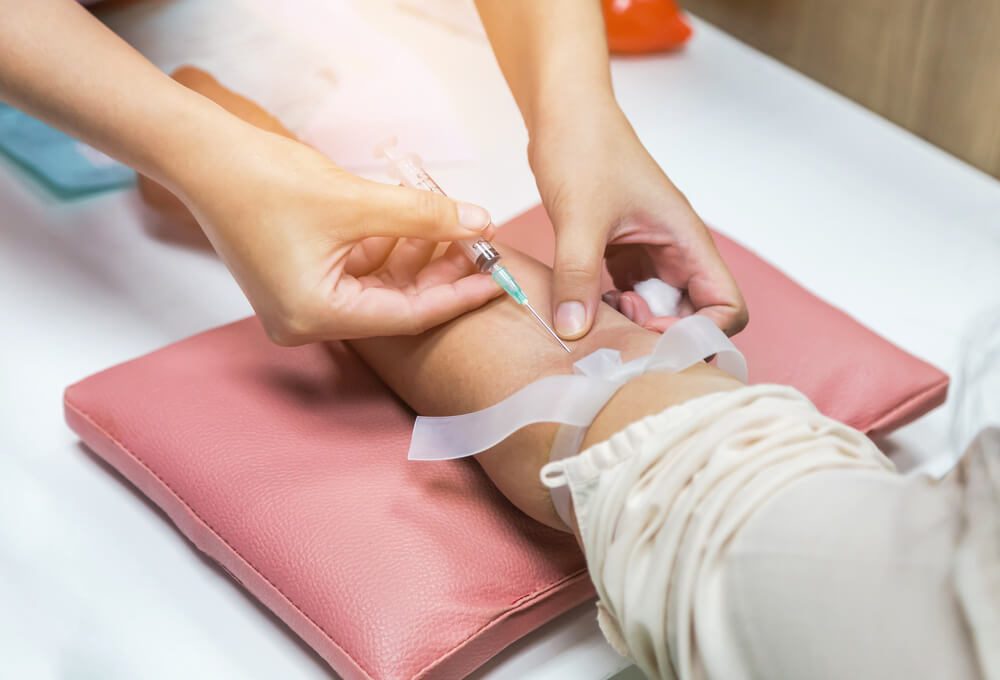 Close up nurse pricking needle syringe in the arm patient drawing blood sample for blood test