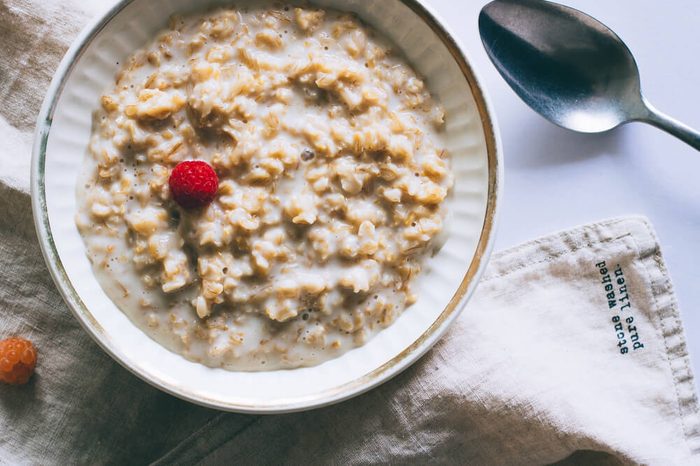 Morning breakfast, oatmeal in milk with raspberries on a white background, top view