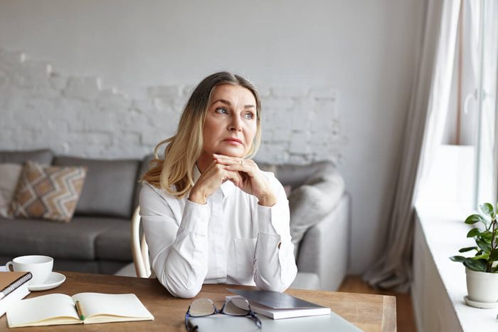 Middle-aged woman sitting at a desk and gazing out the window, deep in thought