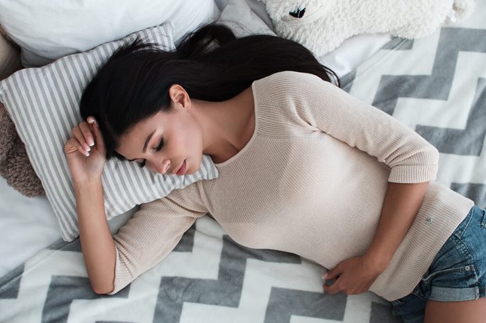 Young woman holding her mid-section as she rests in bed