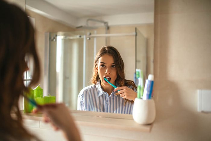 Portrait of a beautiful woman brushing teeth and looking in the mirror in the bathroom.