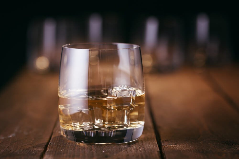 Glass of whiskey with ice cubes on wood table, warm atmosphere, time of relax with whisky with space for text