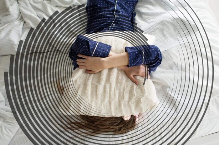 woman in bed on her back, hugging a pillow to her face and chest