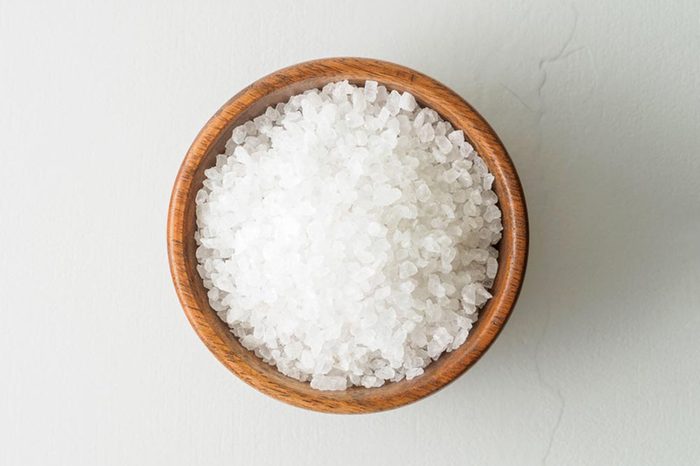 Wooden bowl with large sea salt scrub on gray stone table. 