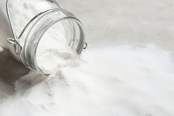 Overturned jar with baking soda on grey background.