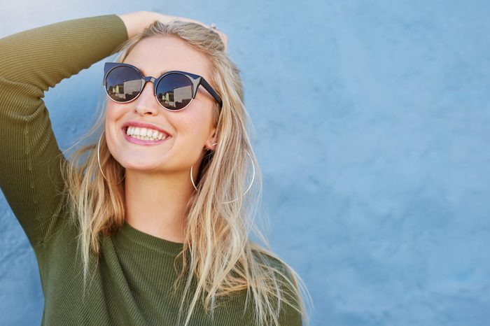 Close up shot of stylish young woman in sunglasses smiling against blue background. Beautiful female model with copy space.