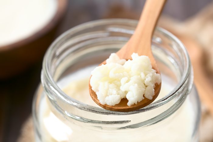 Milk kefir grains on wooden spoon on top of a jar of kefir, photographed with natural light (Selective Focus, Focus in the middle of the kefir grains)