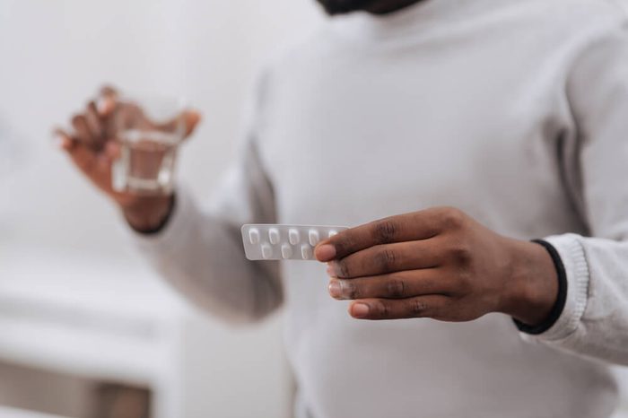 Man holding glass of water and blister pack of medicine