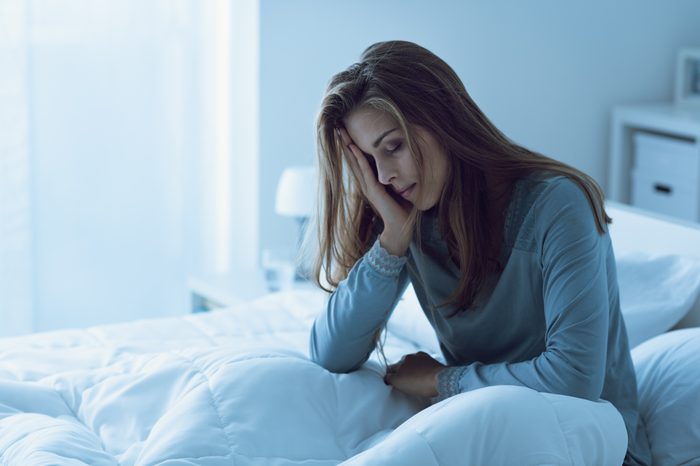 Woman sitting up in bed with her head leaning on her hand