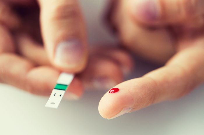 close up of male finger with blood drop and test stripe