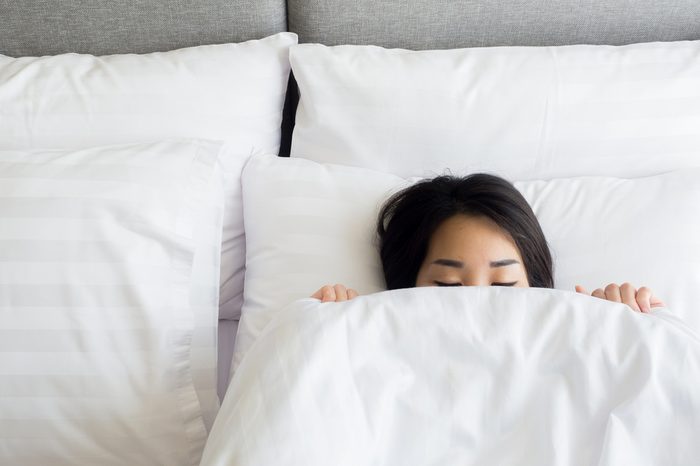 Sleeping woman cover face with blanket flat lay. Close-up of young women, sleeping under white blanket and covering half face.