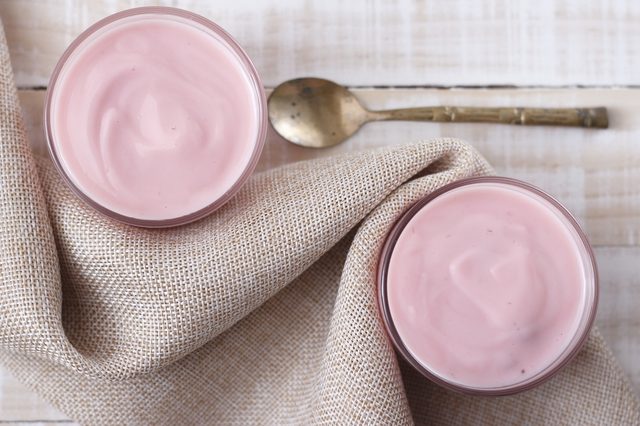 strawberry yogurt in glass with vintage spoon and cloth place on white wooden background. pink yogurt. pink yoghurt, strawberry yoghurt.