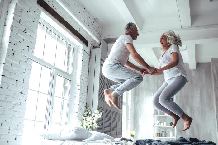 Love lives forever! Senior couple at home. Handsome old man and attractive old woman are enjoying spending time together. Having fun and jumping in bed.