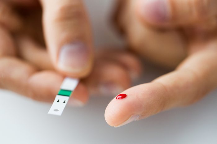 close up of male finger with blood drop and test strip