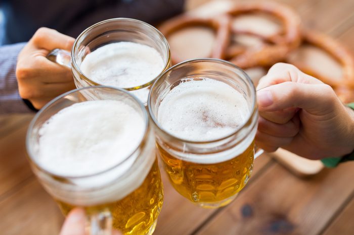 close up of male hands clinking beer mugs at bar or pub