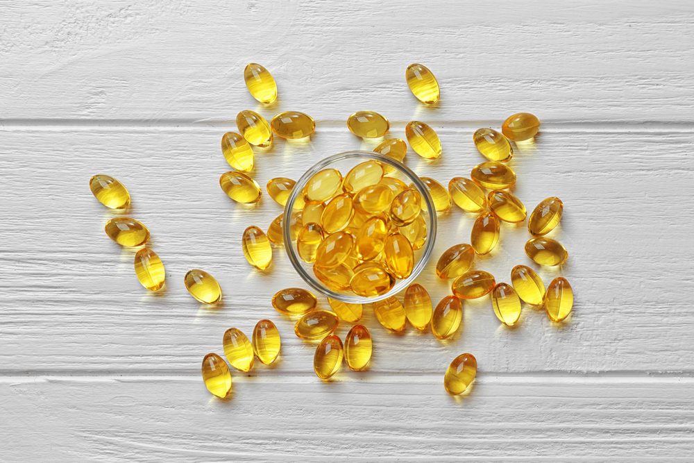 Glass bowl with cod liver oil pills on white wooden table