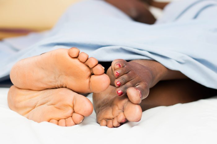 Couple lying in bed and showing their bare feet entwined