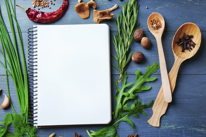 Open recipe book with fresh herbs and spices on wooden background